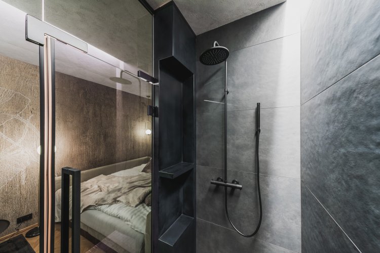 Sprcha ukrytá za černou skleněnou stěnou